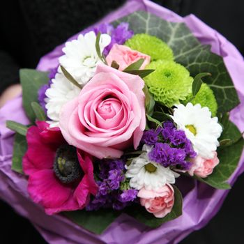 Overhead view of a colourful bouquet of mixed flowers arranged in purple tissue paper to be carried as an accessory at a wedding or celebration