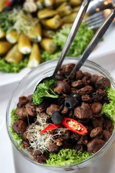 High angle view of assorted cold vegetable dishes on a buffet table with focus to a bowl of fresh roasted or grilled mushrooms garnished with parsley and lettuce