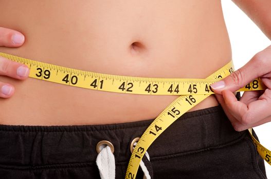 Woman measuring her waist with a yellow measuring tape, isolated in white. Very shallow depth of field. Focus on the hand holding the tape.