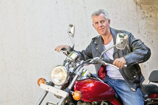 Horizontal take of a senior Caucasian male motorbike rider sat on a red cruiserwearing leather jacket in a relaxed pose. Generic shot location Bombay India