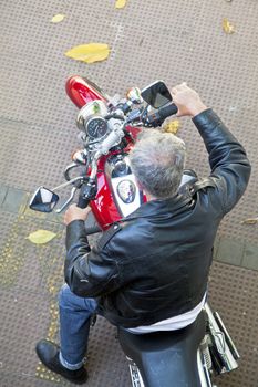 Portrait from an elevated position of a motorcycle, rider in leather jacket and denim jeans on a tiled ground with fallen autumn leaves