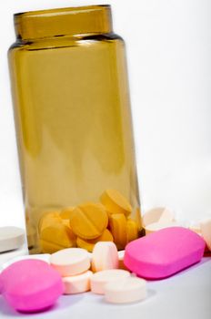 Medicine bottle with purple and yellow pills against white isolated background