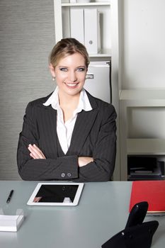 Confident successful businesswoman sitting at her desk with her arms folded smiling at the camera