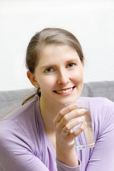Portrait of a young attractive woman smiling holding a glass of water.