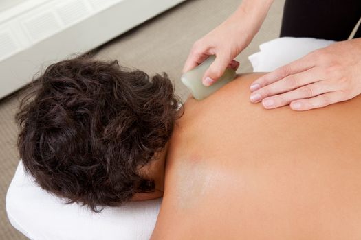Young male receiving Gua Sha treatment on back and shoulders