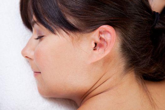 Attractive female relaxing while receiving an acupuncture treatment on the ear
