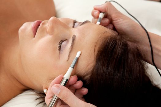 Attractive female patient receiving electro acupuncture on face as part of a anti-aging beauty treatment