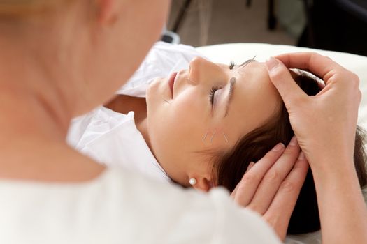 Over the shoulder shot of professional acupuncturist placing needle in face of patient