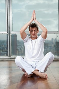 Full length of a young man practicing yoga with hands raised at gym