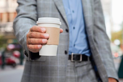 Mid section of businessman holding disposable coffee cup
