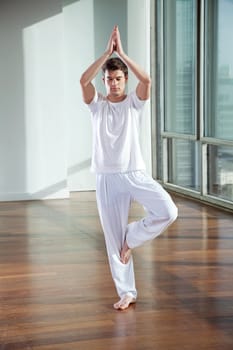 Full length of a young man standing in Tree Pose at gym