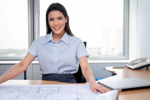 Portrait of pretty female architecture sitting with blueprints on desk