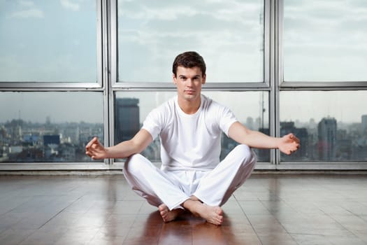 Full length portrait of a young man meditating in lotus position at gym