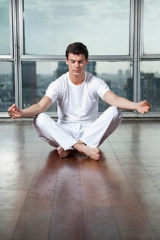 Full length of a young man meditating in lotus position at gym