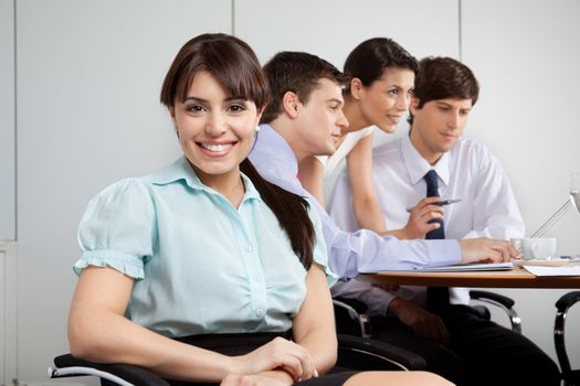 Portrait of cute business woman smiling with team working in background