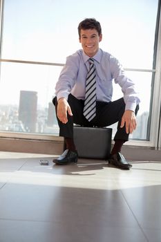 Portrait of handsome young male executive sitting on briefcase