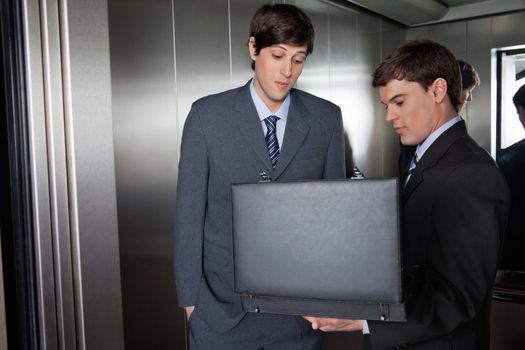 Male in suit showing something in the briefcase to his colleague