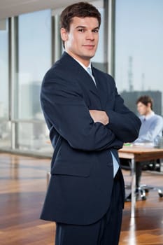 Portrait of confident businessman with arms crossed with colleague working in background