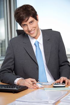 Portrait of young business man calculating budget using calculator at office