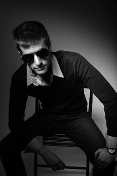 Young man sitting in chair  in sunglasses in shirt in black and white