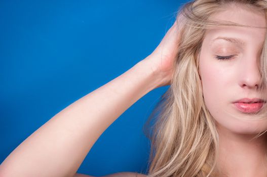 Young blond woman against blue wall closeup