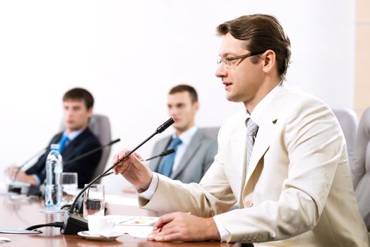 Portrait of a businessman, said into the microphone, in the background colleagues communicate with each other