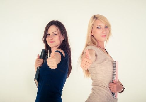 Two beautiful student girls showing thumbs up against white background