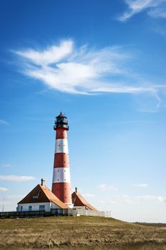 Vertical image of the lighthouse westerhever on a sunny day with blue sky and white clouds.