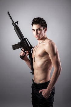 Handsome bare-chested soldier is holding a rifle on black background