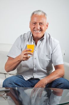 Portrait of happy senior man having glass of fresh orange juice