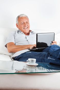 Relaxed senior man sitting on sofa working on laptop at home