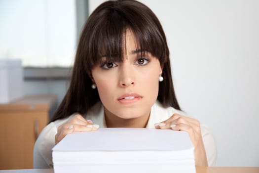 Portrait of overstrained woman at her desk with pile of paperwork