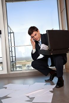 Male entrepreneur bending down to collect scattered papers while talking on cell phone