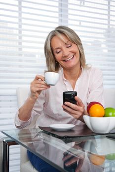 Smiling mature woman using cell phone while having tea