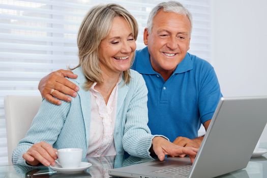 Mature woman having tea and browsing internet with her husband on laptop