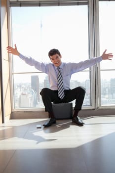Portrait of excited male entrepreneur sitting on briefcase