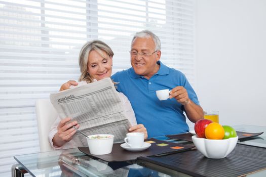 Senior couple reading newspaper while having breakfast