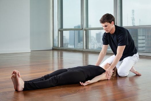 Young male yoga instructor helping female trainee at gym