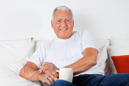 Portrait of relaxed senior man sitting on sofa with warm drink