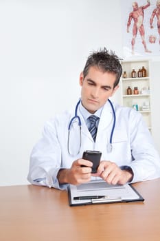 Doctor using mobile phone, sitting at desk .