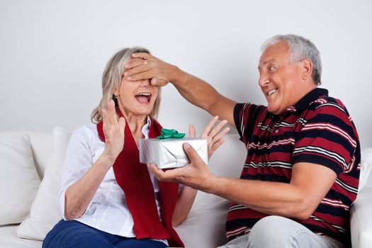 Senior man covering his wife's eyes to surprise her with a gift