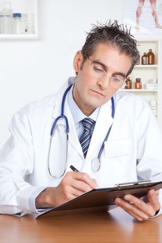Doctor writing on clipboard sitting at desk.