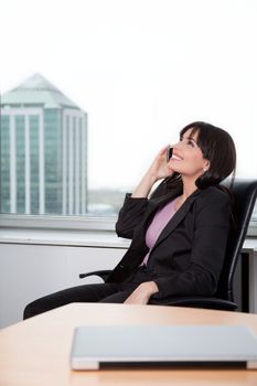 Young Woman Relaxed In Chair And Talking On Cell Phone In Office.