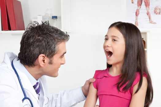 Happy male doctor examining child mouth in clinic.