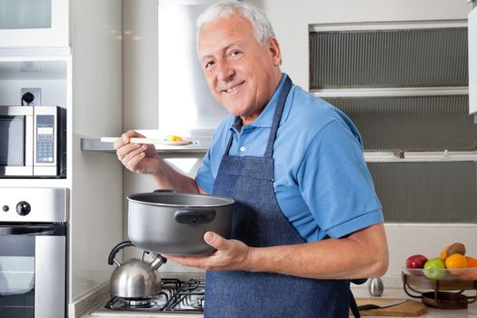 Portrait of smiling senior man holding spoon to taste food