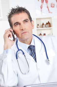 Doctor talking on mobile phone, sitting at desk .