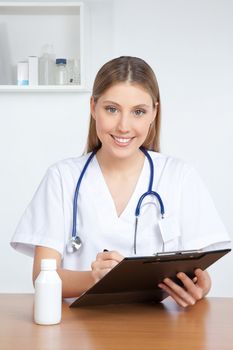 Happy smiling female doctor writing on clipboard.