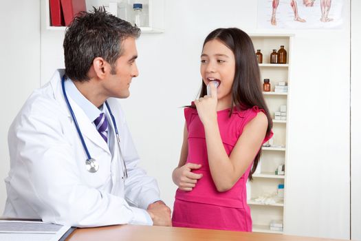 Young little girl using asthma inhaler in front of doctor.
