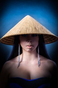 Beauty Portrait. Beautiful brunette Asian woman with long black hair wears vietnam hat. Shot in a studio on a black background