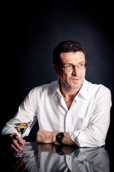 adult man holding an alcoholic drink thoughtful on black background